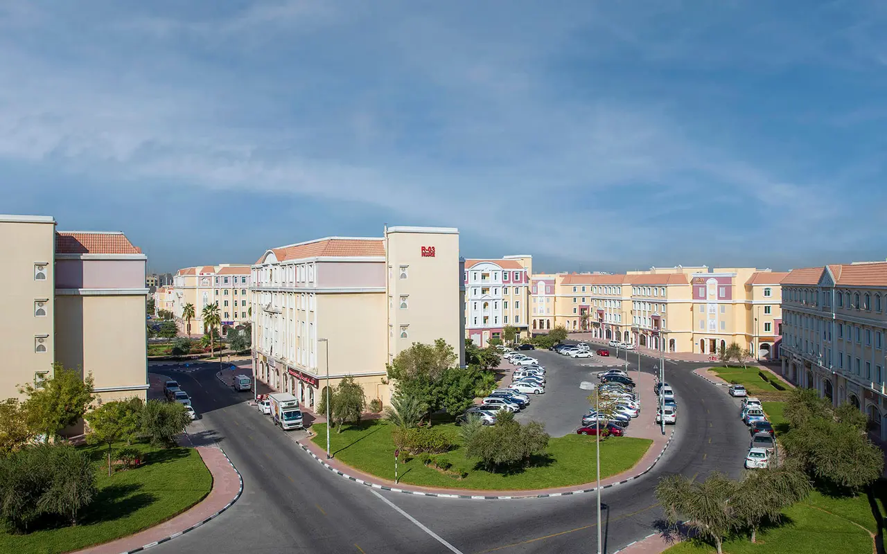 International City, street-level residential buildings and landscaped roundabout. Area context, not a photograph of L-04.