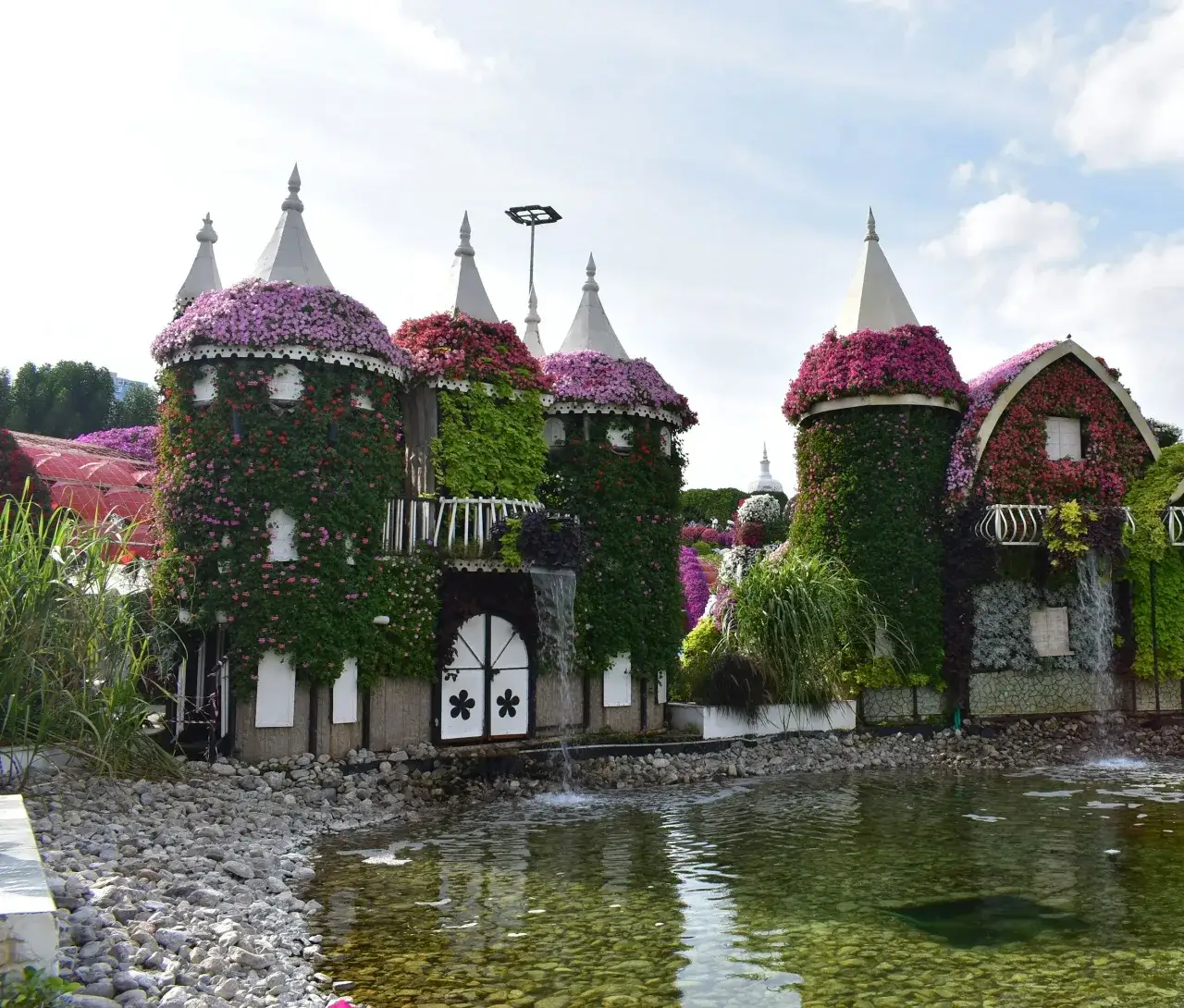 Flower-covered houses and water feature at Dubai Miracle Garden in Arjan. Area context, not a photograph of Vincitore Volare.